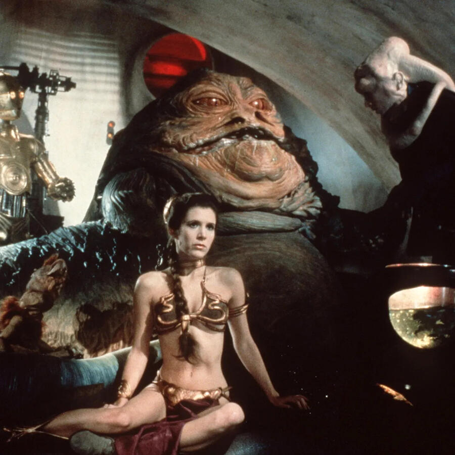 A screenshot from Star Wars Episode 6 of Leia Organa in a metal bikini top and a loincloth that is reminiscent to a belly dancer's outfit.